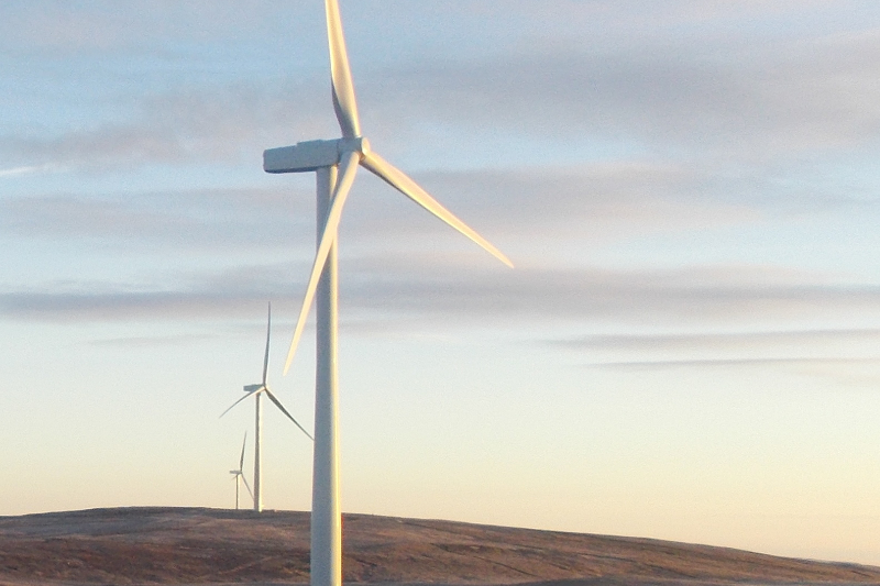 Drei Windräder auf einer Wiese bei untergehender Sonne.