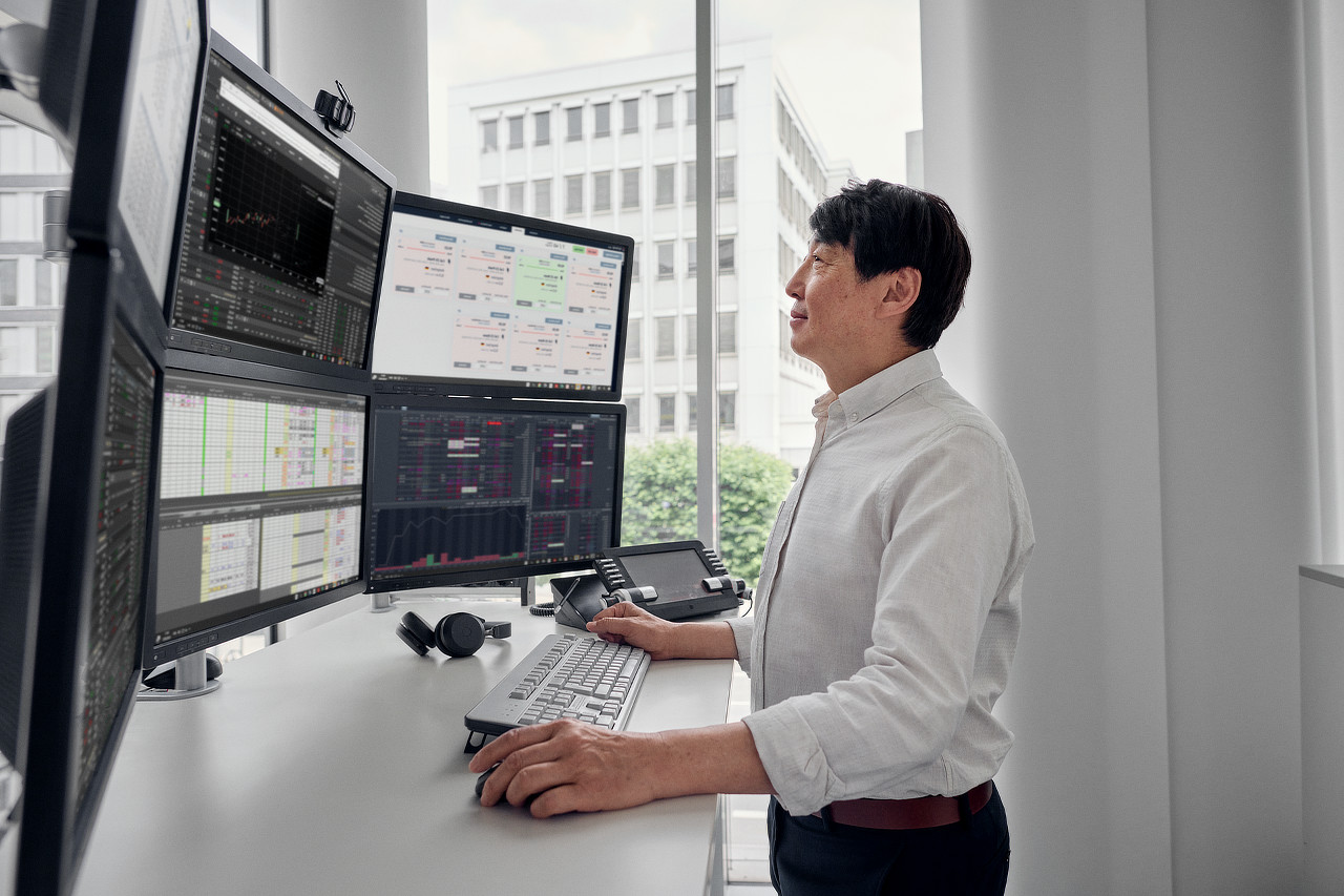 Ein Mann steht an einem Schreibtisch mit 6 Bildschirmen und schaut darauf.