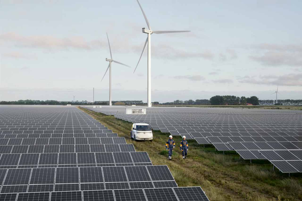2 Personen laufen durch einen Solarpark. Im Hintergrund stehen Windräder.