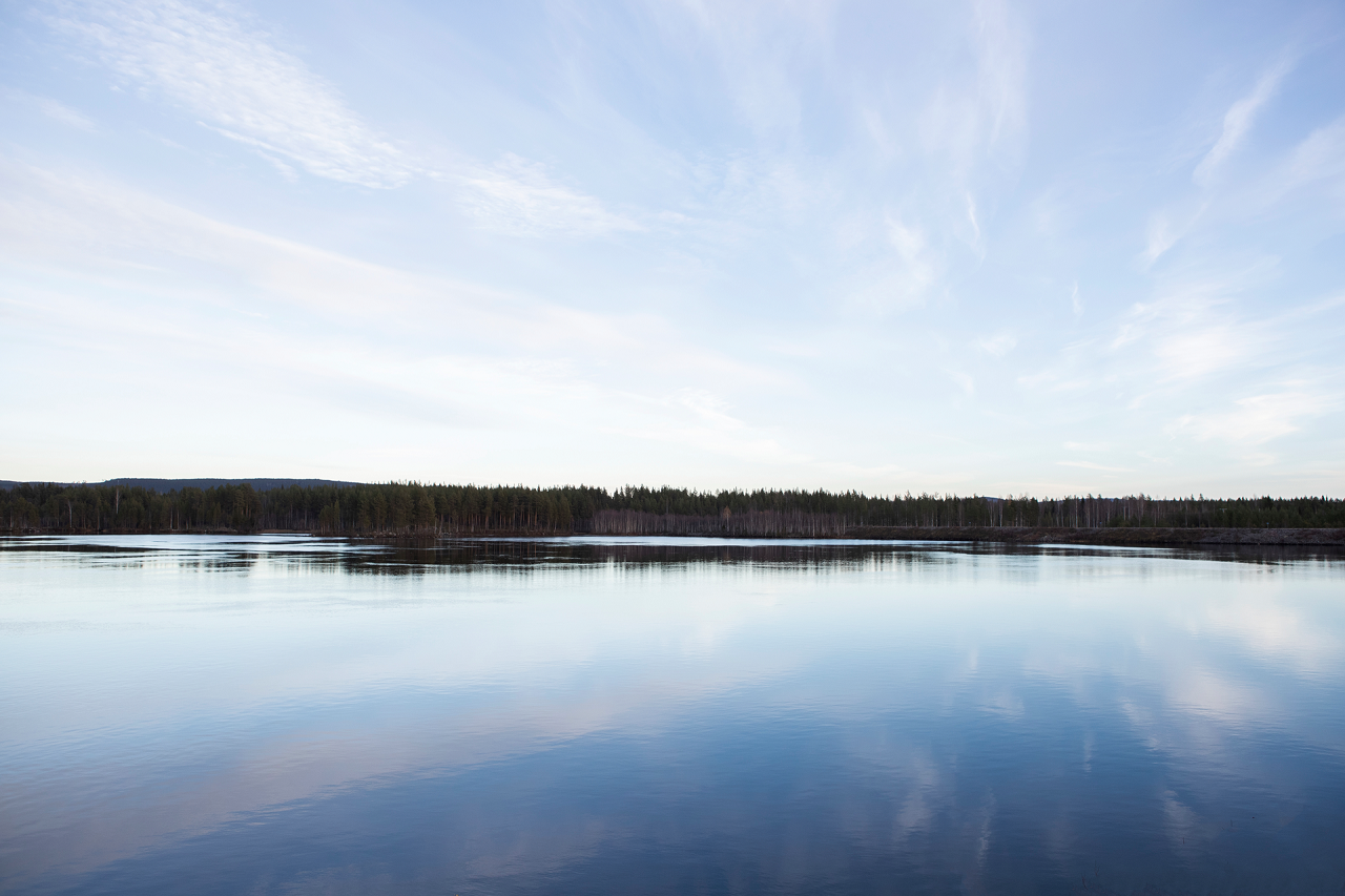 Der Wald und blauer Himmel spiegeln sich in einem ruhigen See.