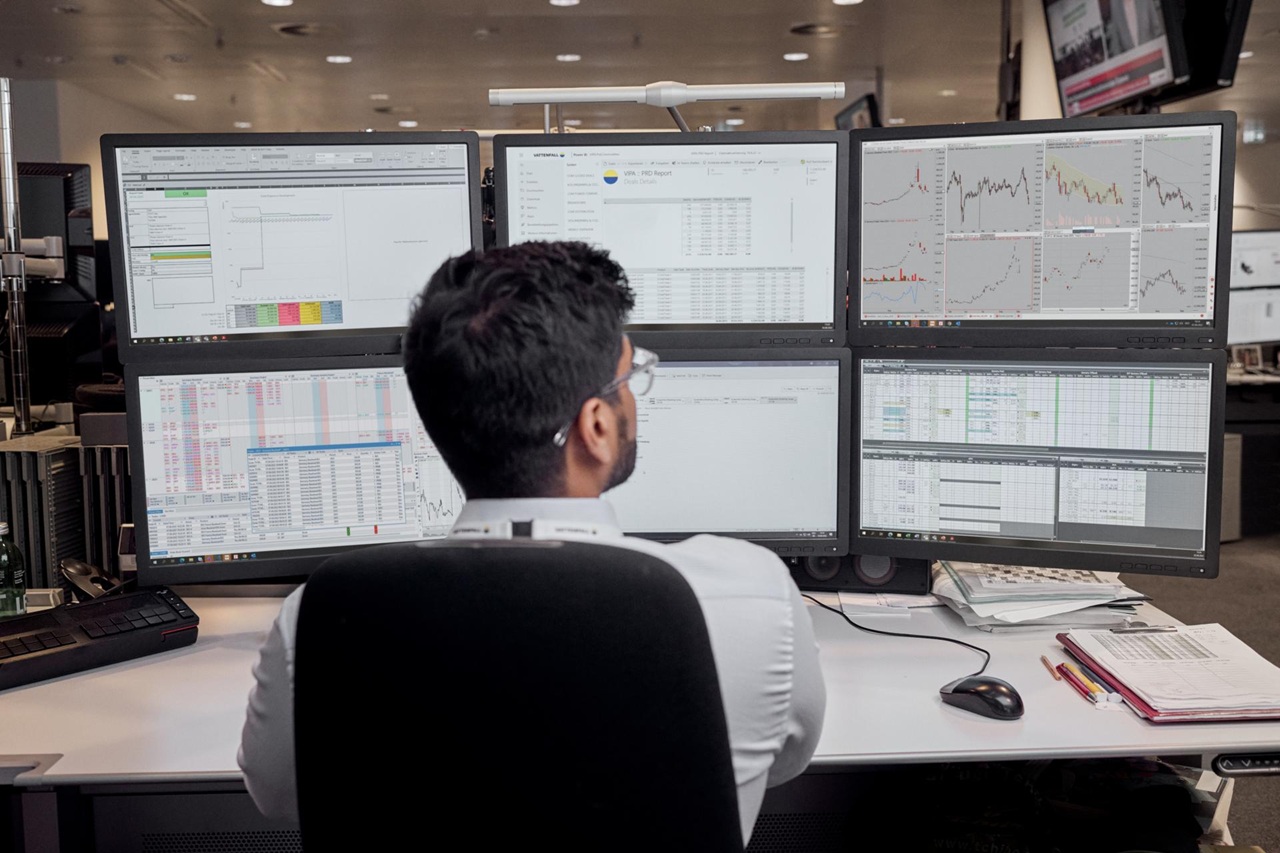 Working employee infront of six screens with different graphics on those