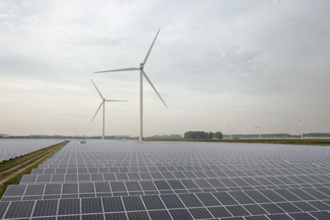 Im Vordergrund ist ein Solarpark, dahinter stehen zwei Windräder
