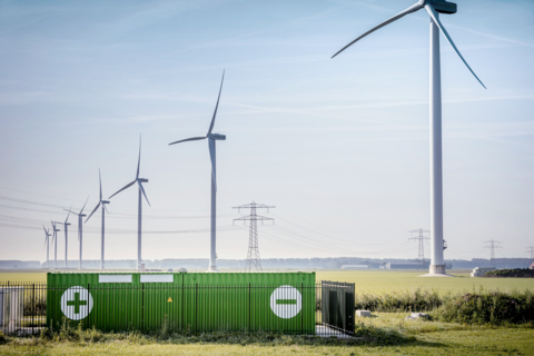 Batteriespeicher vor einem Windpark bei blauem Himmel