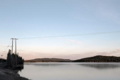  Stimmungsvolles Bild im Morgengrauen mit Blick auf einen See und oberirdischen Stromkabeln