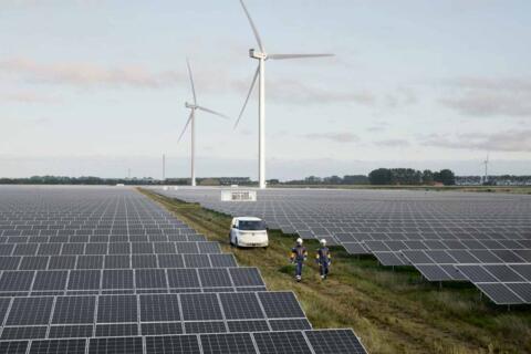 2 Personen laufen durch einen Solarpark. Im Hintergrund stehen Windräder.