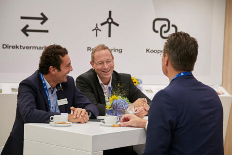 Drei Mitarbeiter Vattenfalls in Anzügen auf der Messe, die gemeinsam lachen.