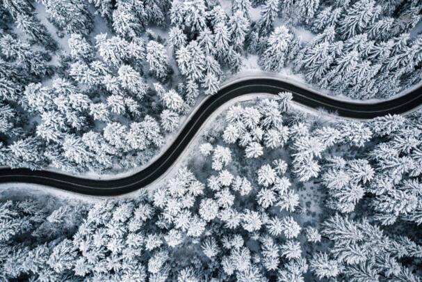 Luftaufnahme von einer Straße, die durch einen verschneiten Wald führt.