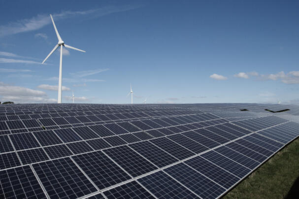 Ein Solarpark, bei dem im Hintergrund Windräder zu sehen sind.