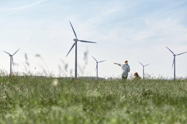 Zwei Frauen auf einer Wiese, die in die Ferne zu den Windrädern schauen.