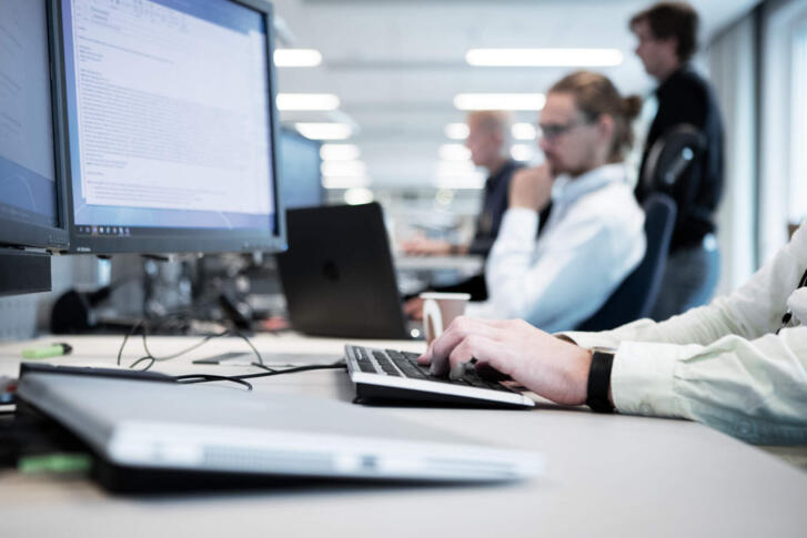 Mehrere Menschen, die im Büro an ihren Computern sitzen.