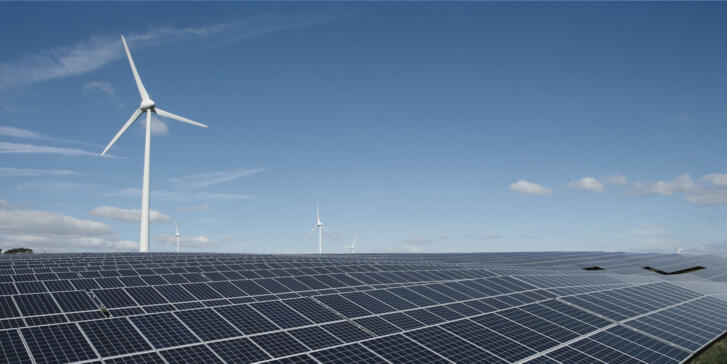 Ein Solarpark, bei dem im Hintergrund Windräder zu sehen sind.