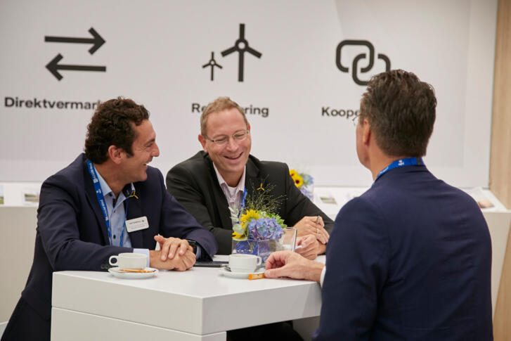 Drei Mitarbeiter Vattenfalls in Anzügen auf der Messe, die gemeinsam lachen.