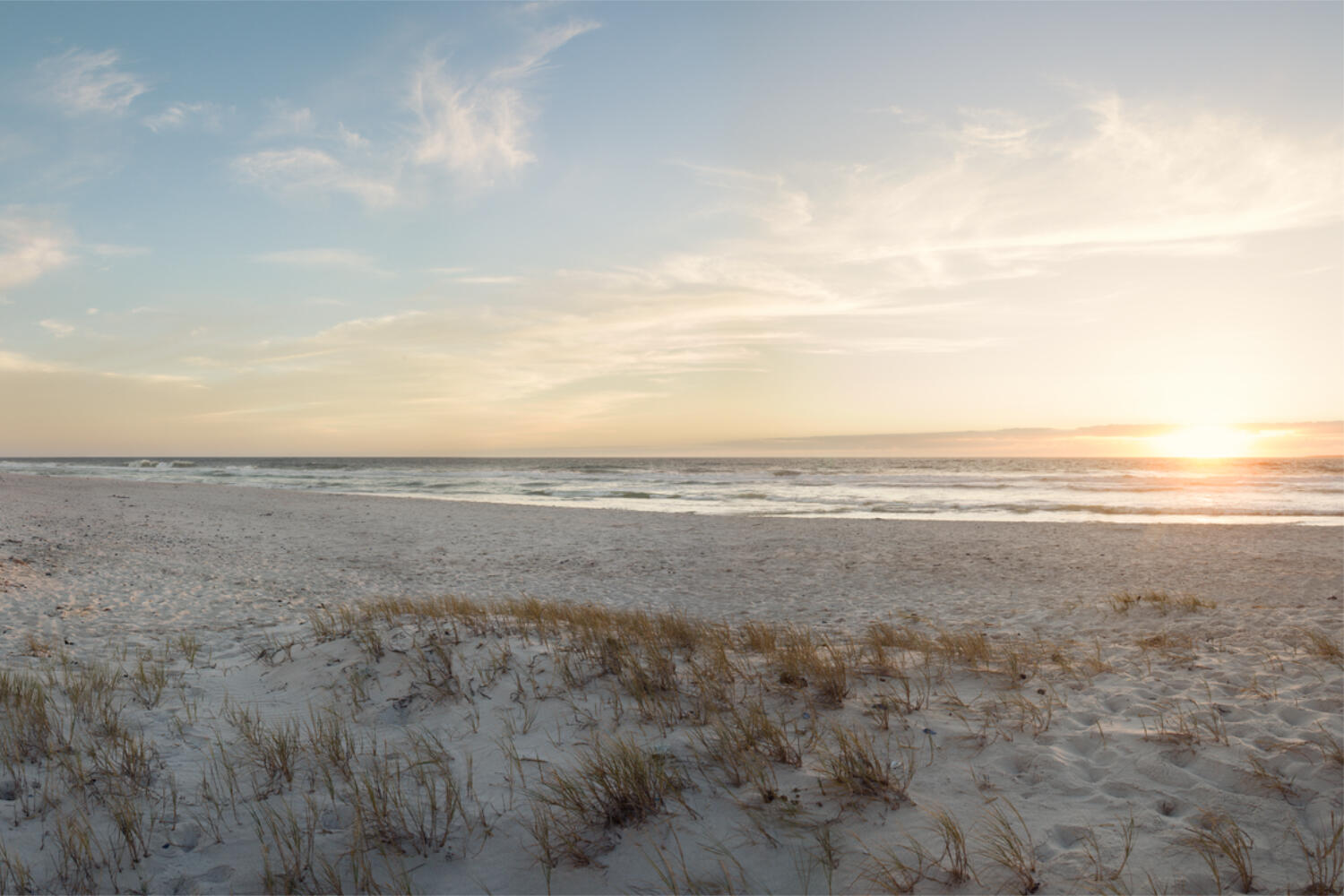Ein Strand mit Dünen, das Meer im Hintergrund bei einem Sonnenuntergang