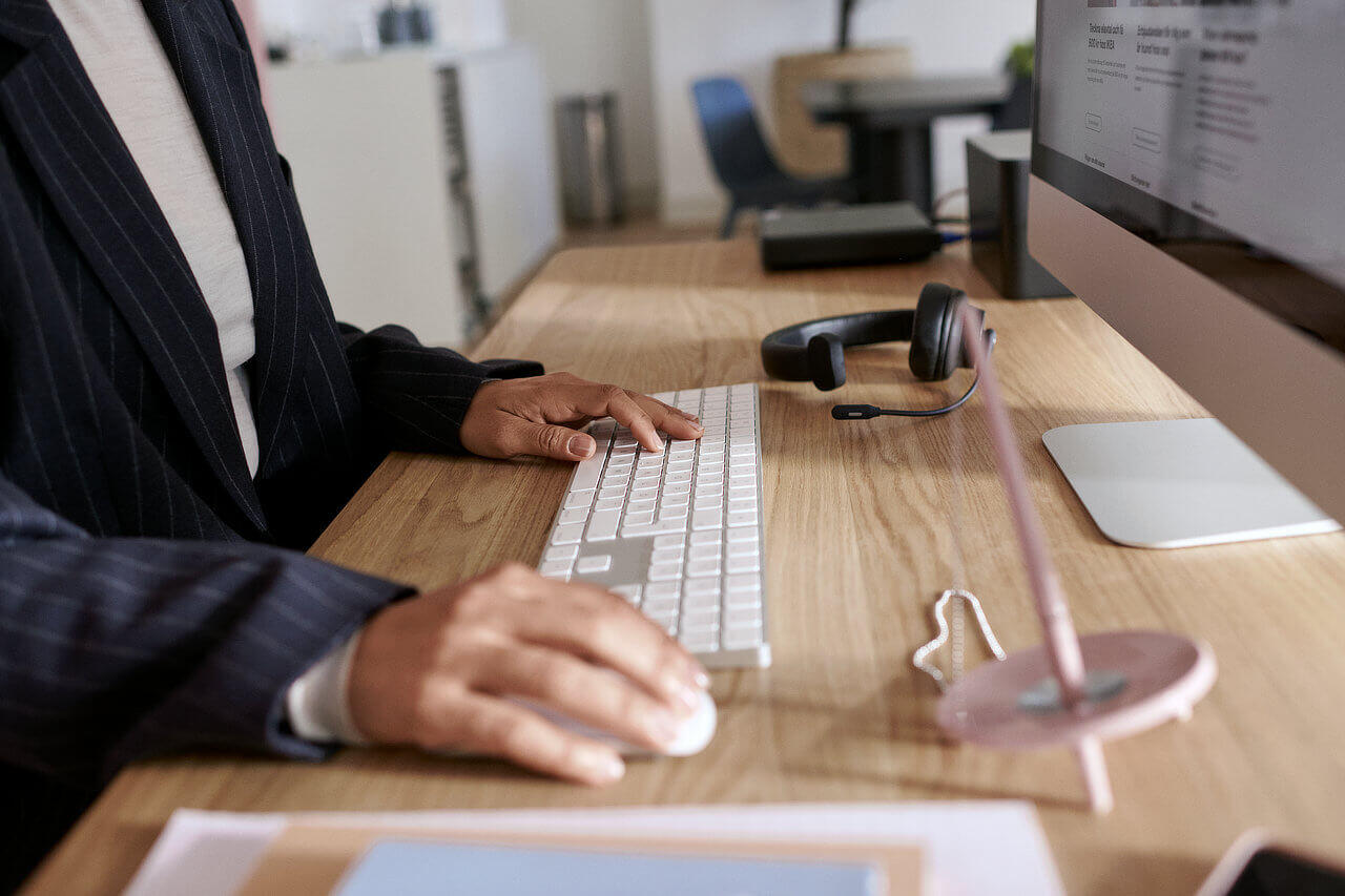 Eine Person sitzt an einem Schreibtisch, die Hände an einer Tastatur, vor ihr steht ein Monitor.