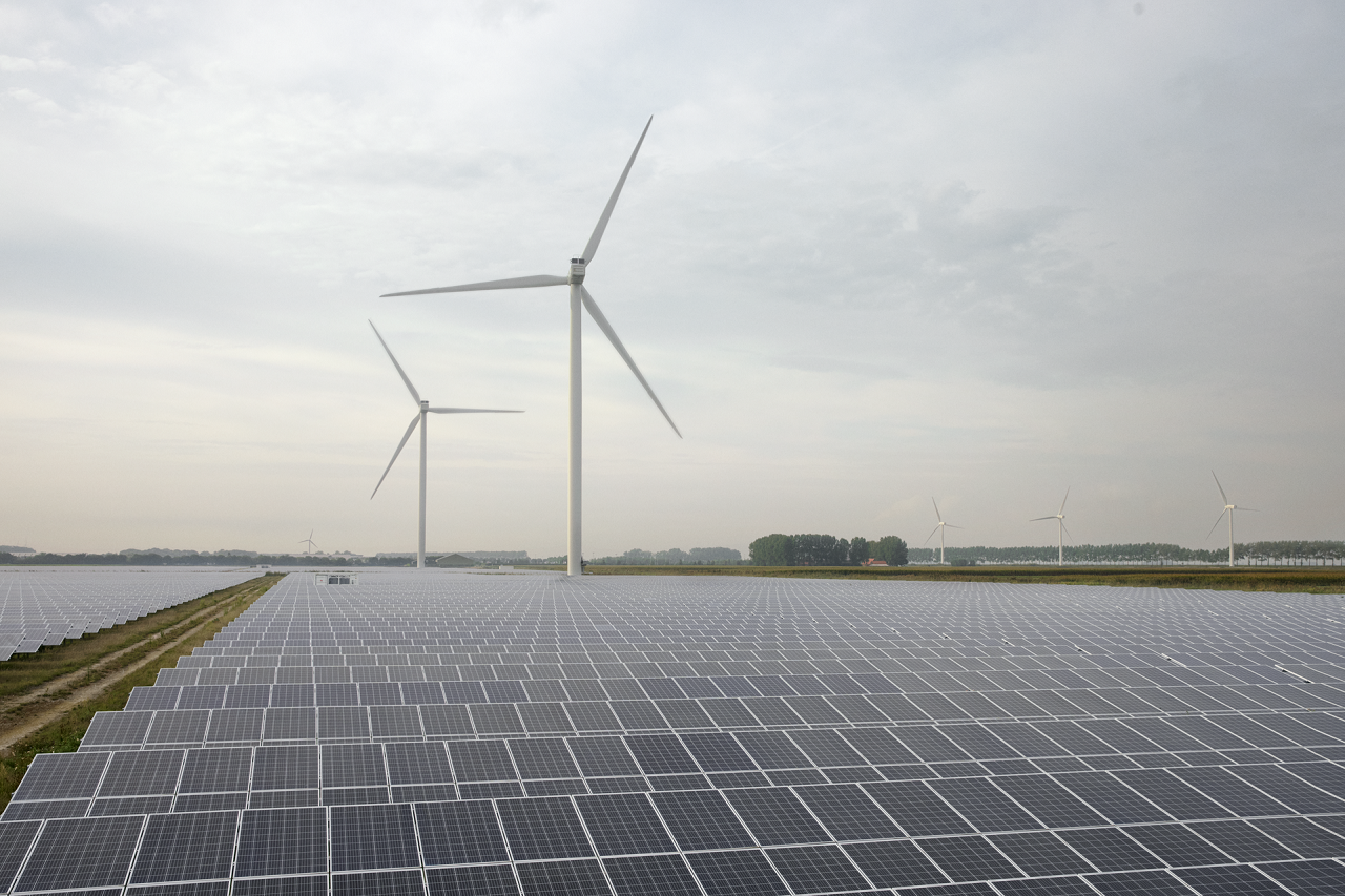 Im Vordergrund ist ein Solarpark, dahinter stehen zwei Windräder