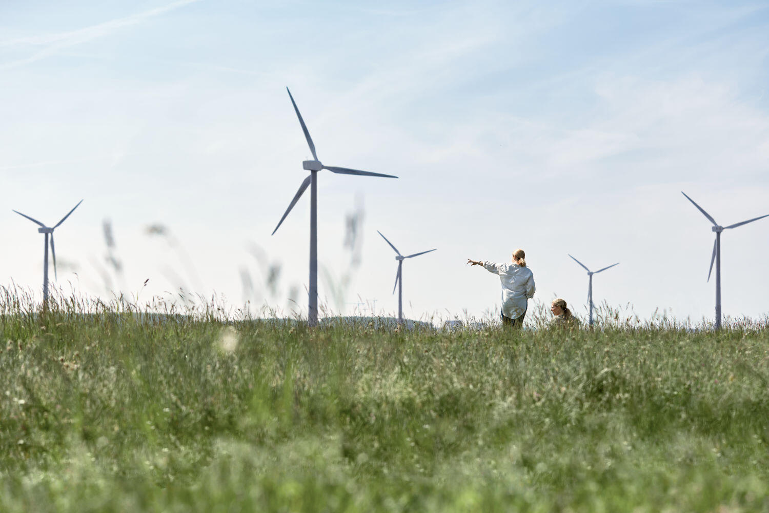 Zwei Frauen auf einer Wiese, die in die Ferne zu den Windrädern schauen.