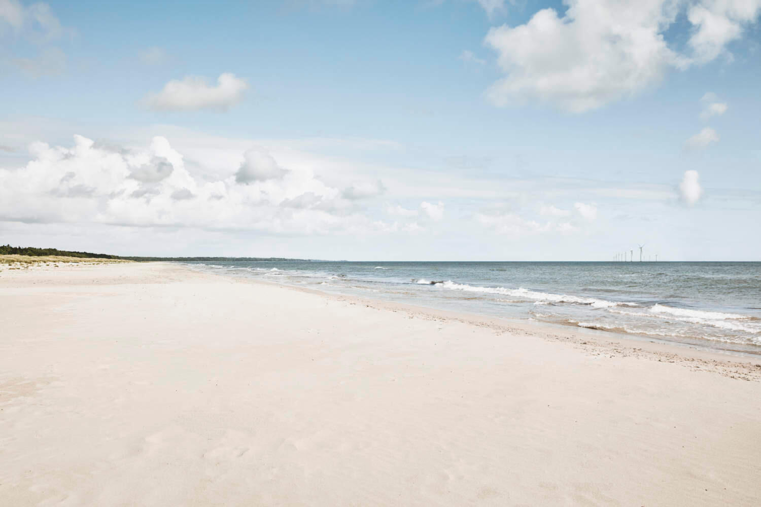 Strand und Meer. Am Horizont im Meer ist ein Offshore-Windpark zu sehen.