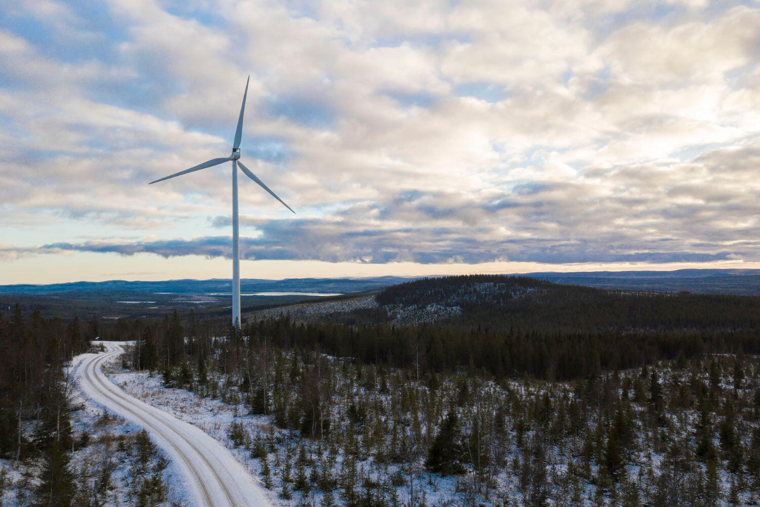 Eine Landschaft, welche leicht mit Schnee bedeckt ist. Im Hintergrund befindet sich ein Windrad.
