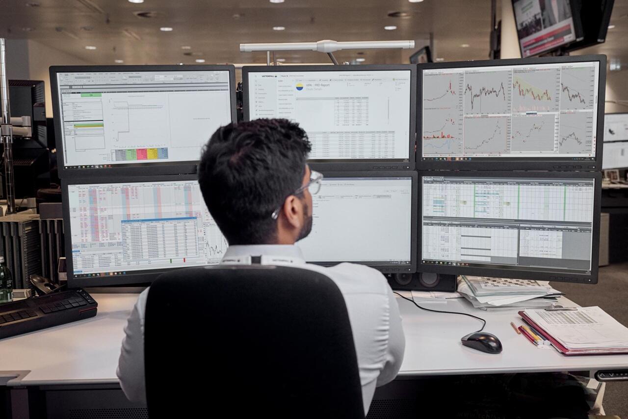 Working employee infront of six screens with different graphics on those